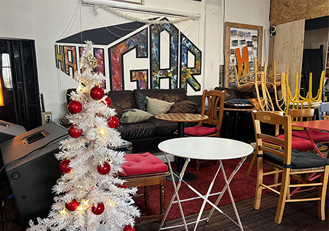 sapin de noël au premier plan chaises et tables au second plan canapé en arrière-plan et fresque en volume avec l'inscription " Hangar"